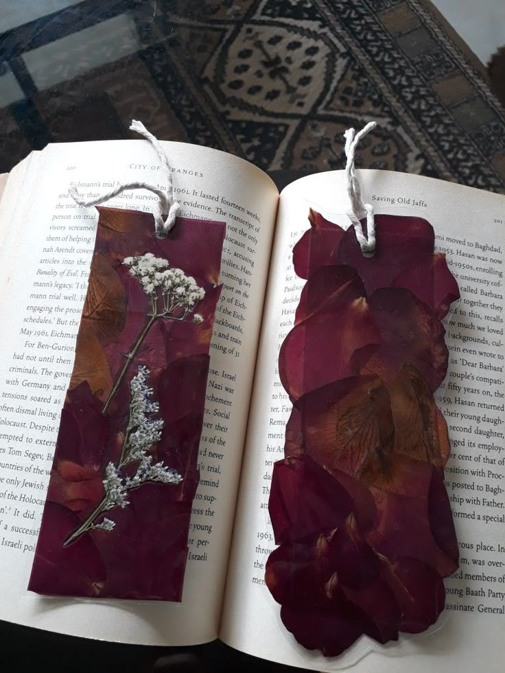 an open book with two tags attached to it and flowers on the pages, sitting on a table