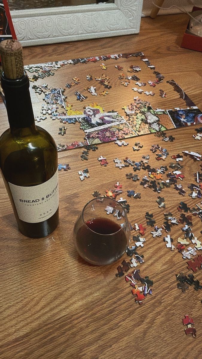 a bottle of wine sitting on top of a wooden table next to a jigsaw puzzle