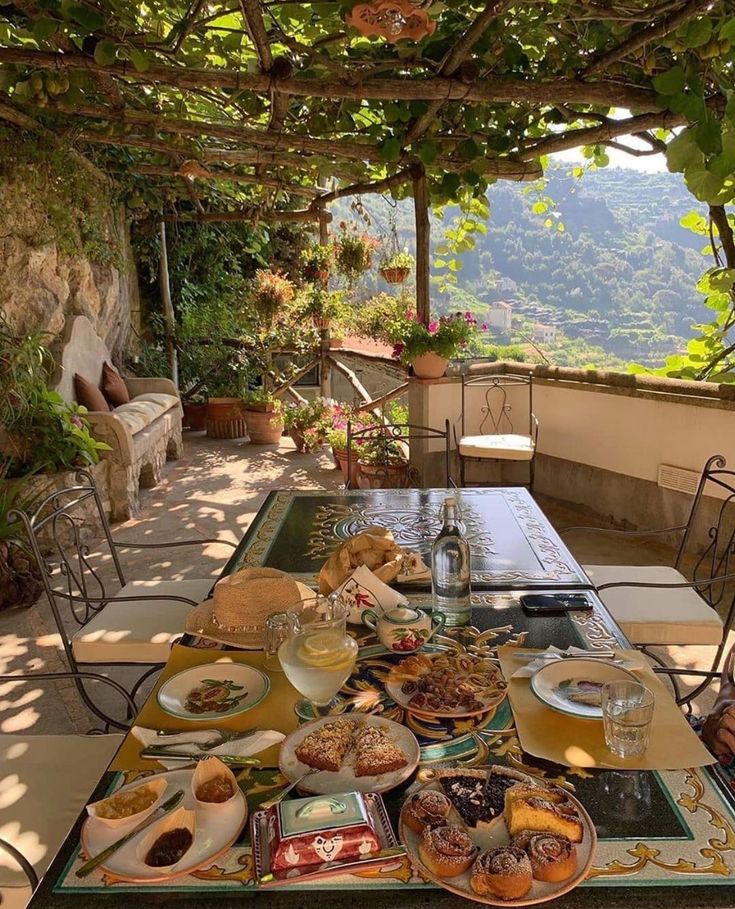 an outdoor table with food and drinks on it in front of a stone wall covered patio