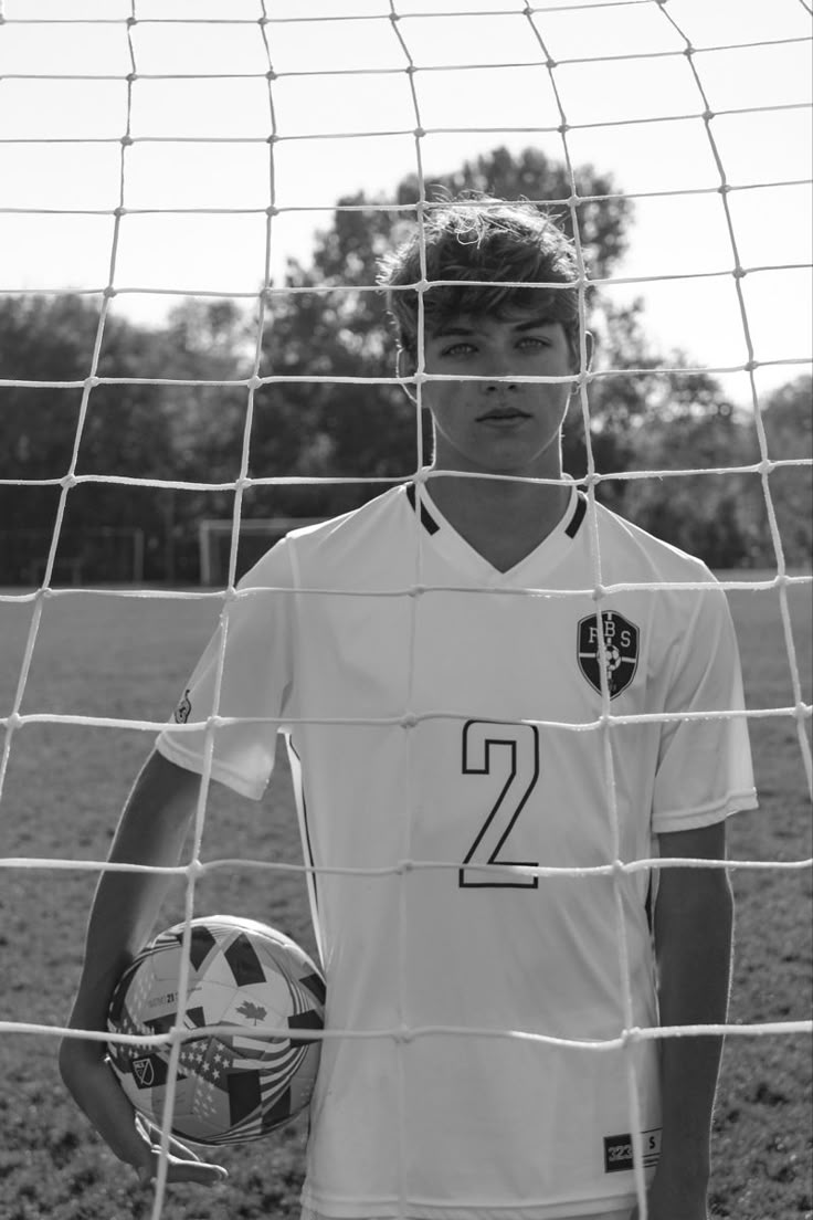 a young man standing in front of a soccer net holding a ball and wearing a number two jersey