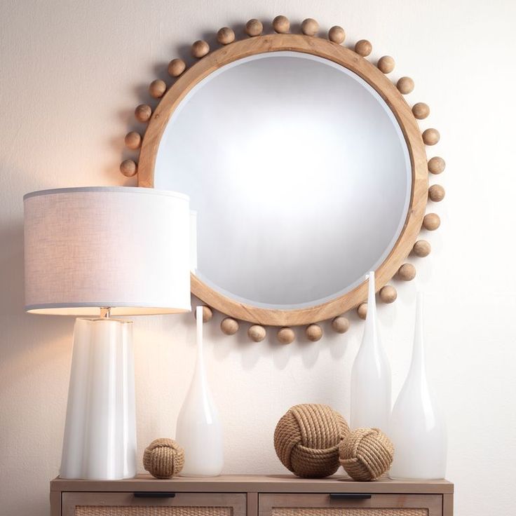 a round mirror sitting on top of a wooden dresser next to a lamp and vase