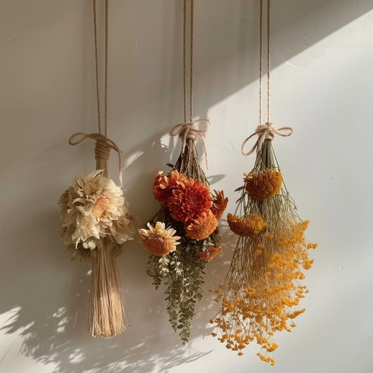 three dried flowers hanging from strings on a wall