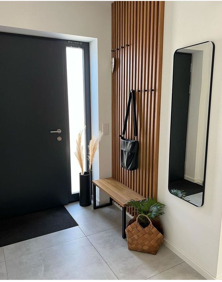 a wooden bench sitting in front of a black door next to a mirror and potted plant