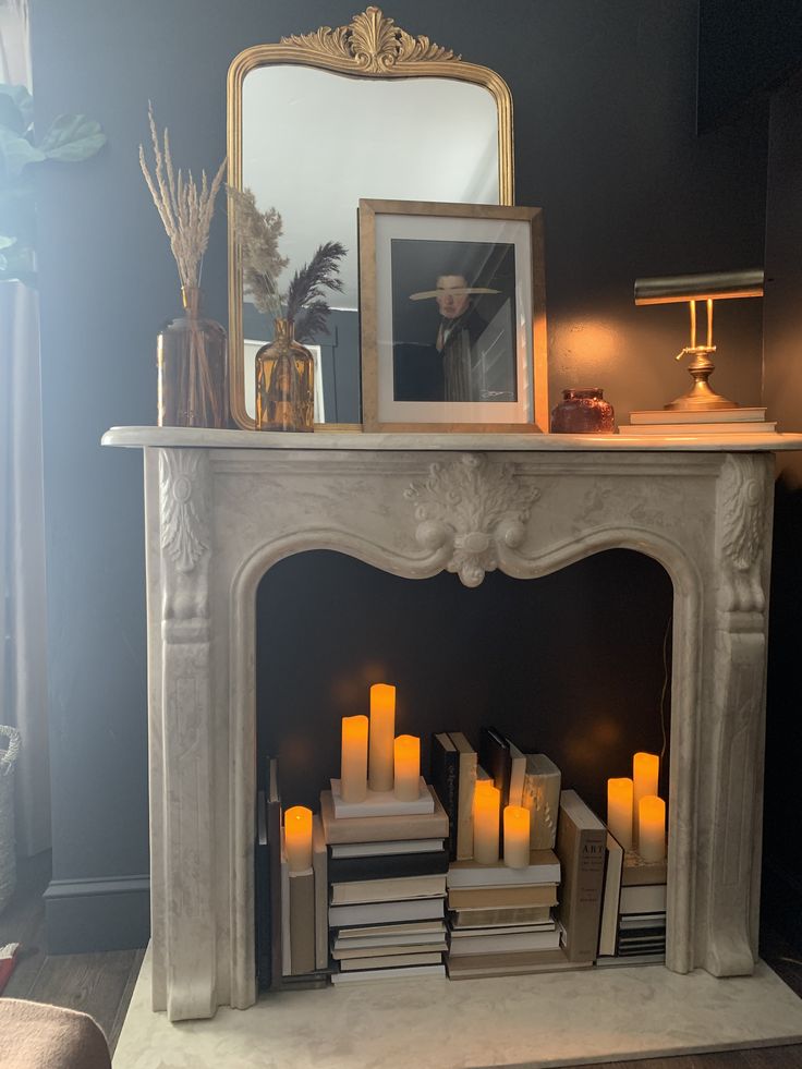 a fire place with books and candles in front of the fireplace, next to a mirror