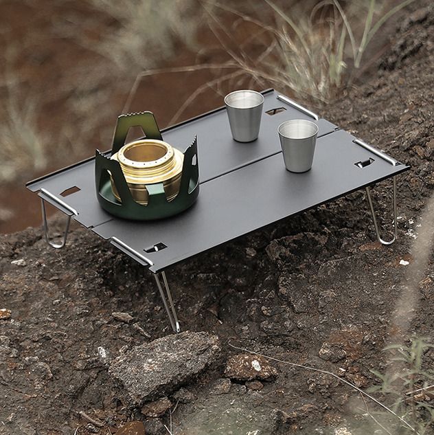 a table with two cups on it sitting in the middle of a dirt field next to some grass