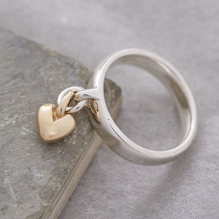 Add charm to your jewellery collection with our exquisite and unique solid silver ring, adorned with a delicate sweetheart recycled gold heart charm that gracefully sways with your every move. This everyday yet extraordinary ring is destined to spark conversations and become a cherished part of your personal style. Craftsmanship: Meticulously crafted using traditional lost wax casting techniques, our solid sterling silver rings are designed for both aesthetics and comfort. The ring features a robust and enduring loop on the front, while its generous band shape prioritizes comfort, durability, and contemporary elegance. The dangling heart charm is crafted from your choice of either recycled solid rose gold, or recycled solid yellow gold, with a beautifully rounded, organic shape. Quality As Ring With Charms, Charm Rings Dangle, Chunky Silver Rings, Charm Ring, Gold Heart Ring, Unusual Rings, Silver Signet Ring, Rose Gold Heart, Designer Fashion Jewelry