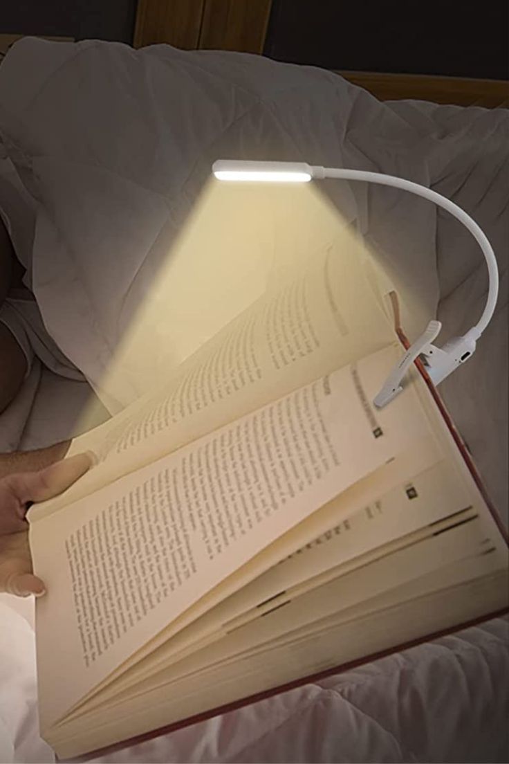 a man laying in bed reading a book with a lamp on top of his head