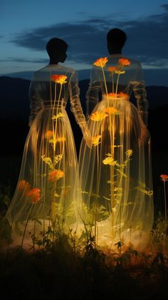 two people standing next to each other with flowers in their hands and lights on them