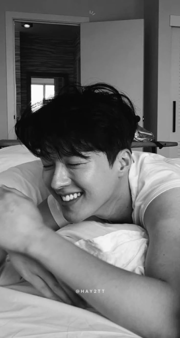 a young man laying in bed smiling at the camera