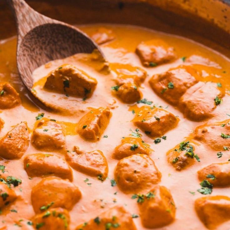 a wooden spoon in a pot filled with meatballs and gravy, topped with parsley