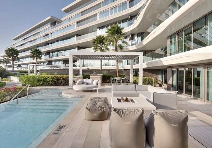 an outdoor lounge area next to a swimming pool in front of a large apartment building