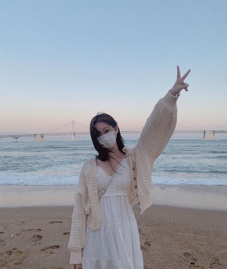 a woman wearing a face mask standing on the beach with her hands in the air