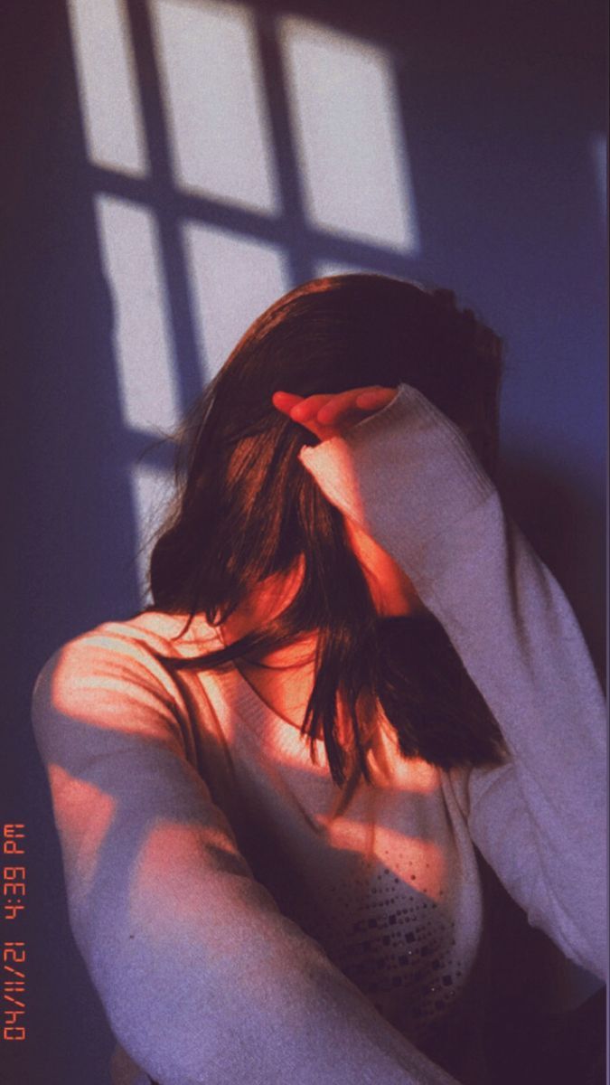 a woman standing in front of a window with her hands on her head and arms behind her head