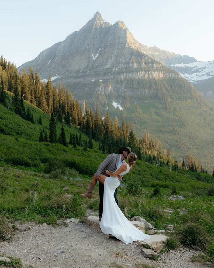 a bride and groom kissing on the side of a mountain with trees in the background