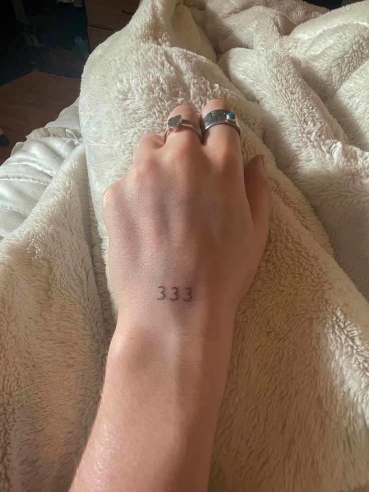 a person's hand with a small tattoo on their left wrist, resting on a blanket