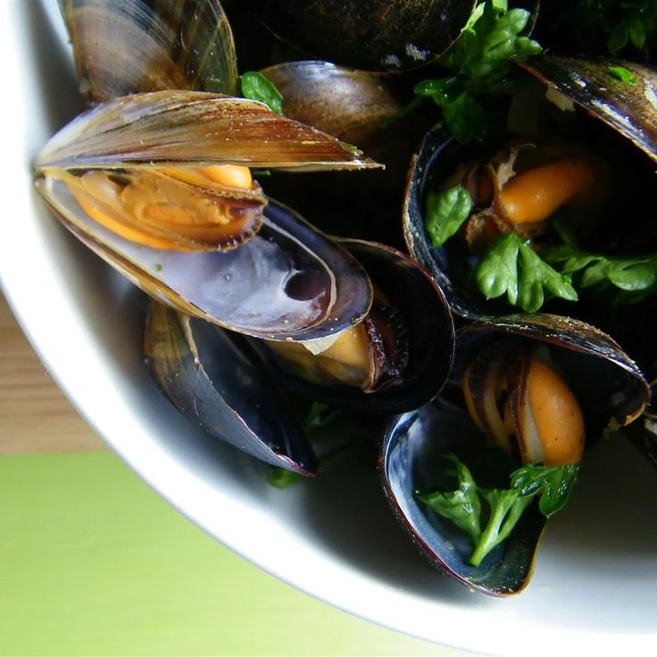 a white bowl filled with mussels and greens