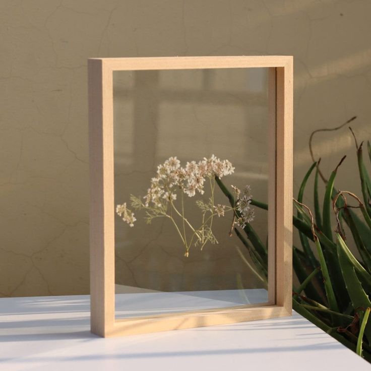 a wooden frame with flowers in it sitting on a table next to a potted plant