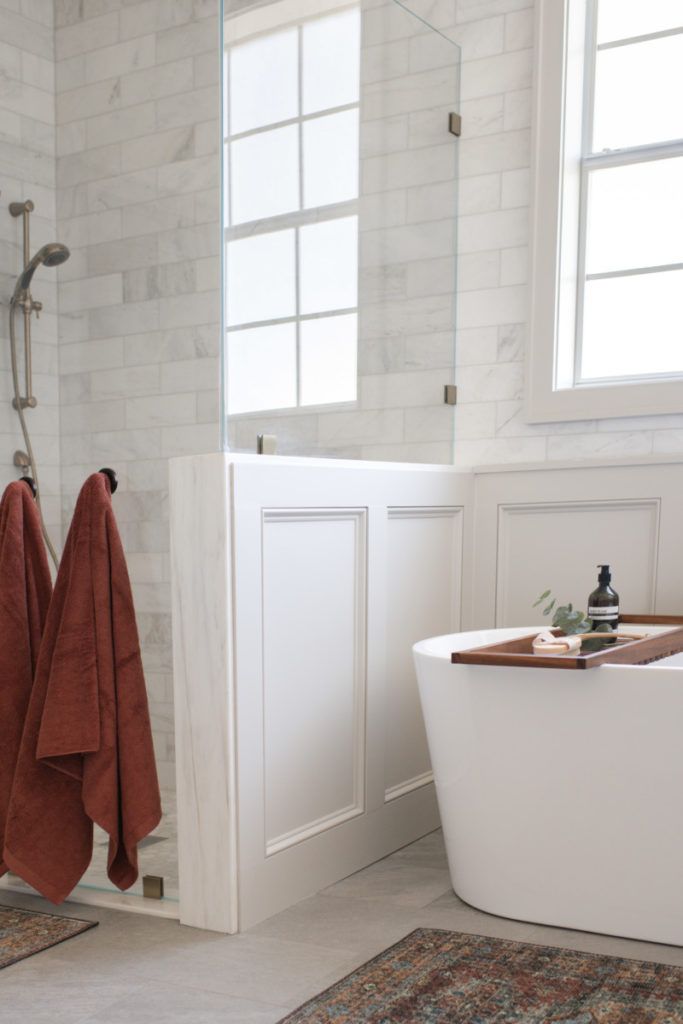 a white bathtub sitting next to a window in a bathroom with a rug on the floor