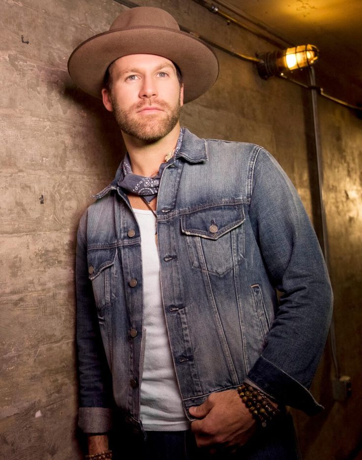 a man wearing a cowboy hat standing in front of a wall with his hands on his hips