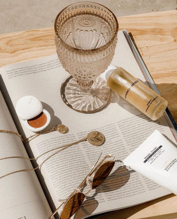 an open book with sunglasses, sunscreen and other items sitting on top of it