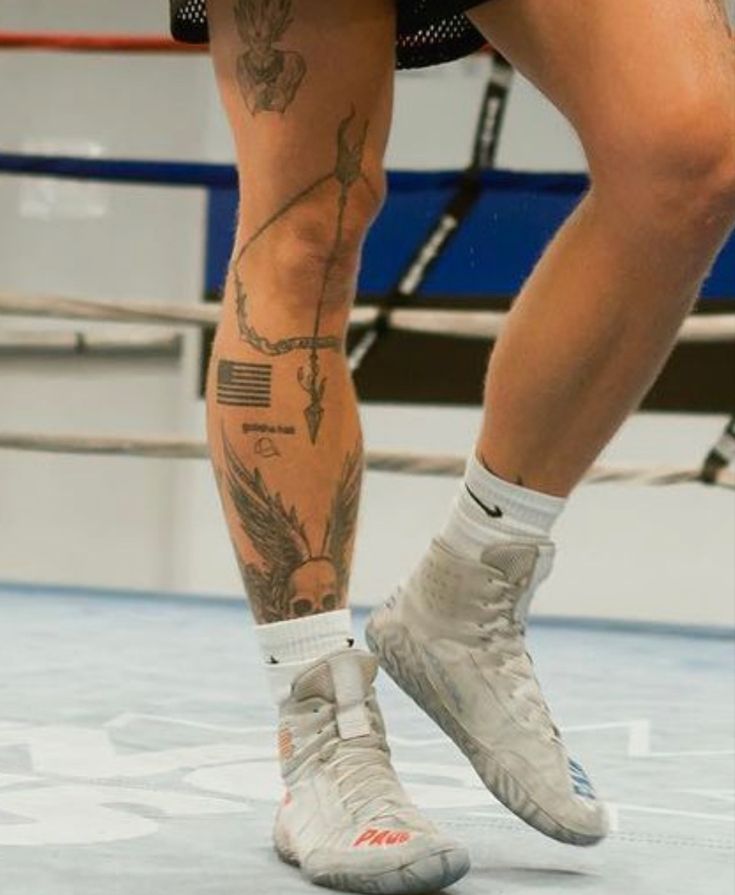 a man with tattoos on his legs and feet standing in front of a boxing ring