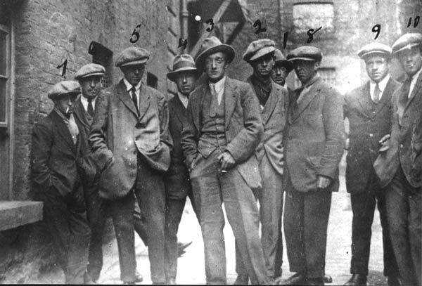 a group of men standing next to each other in front of a stone wall with numbers on it