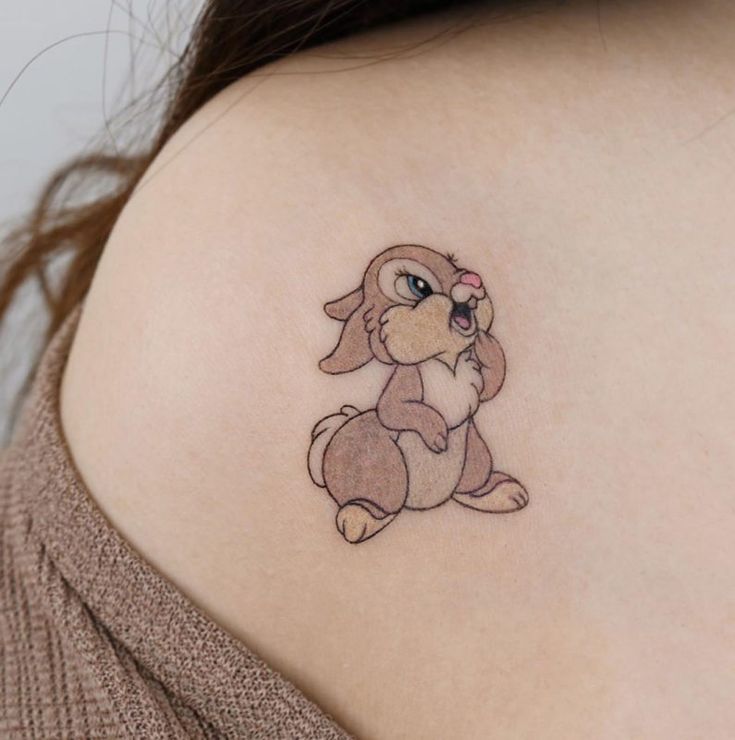 a woman with a small tattoo on her back shoulder, holding a teddy bear in one hand