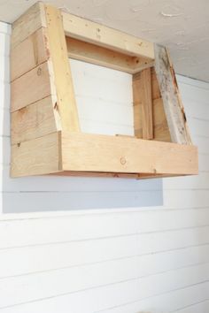 a wooden window frame hanging on the side of a white wall with wood planks