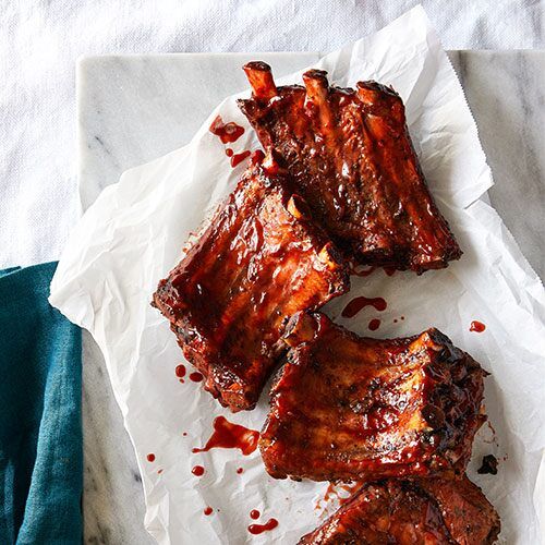 three pieces of ribs on top of paper next to a knife and fork with sauce