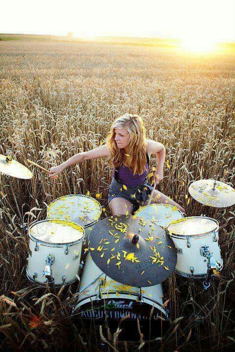 a woman sitting on top of a drum set in a field