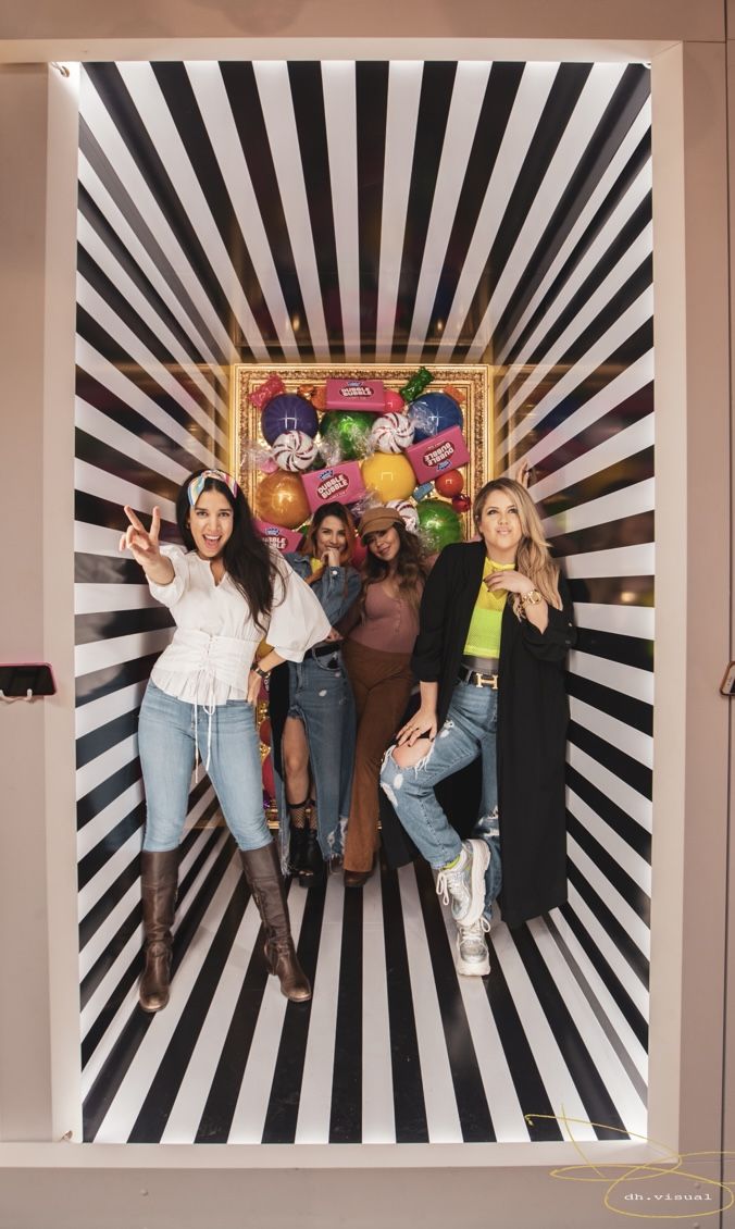 three women standing in front of a photo booth with balloons and streamers on the wall