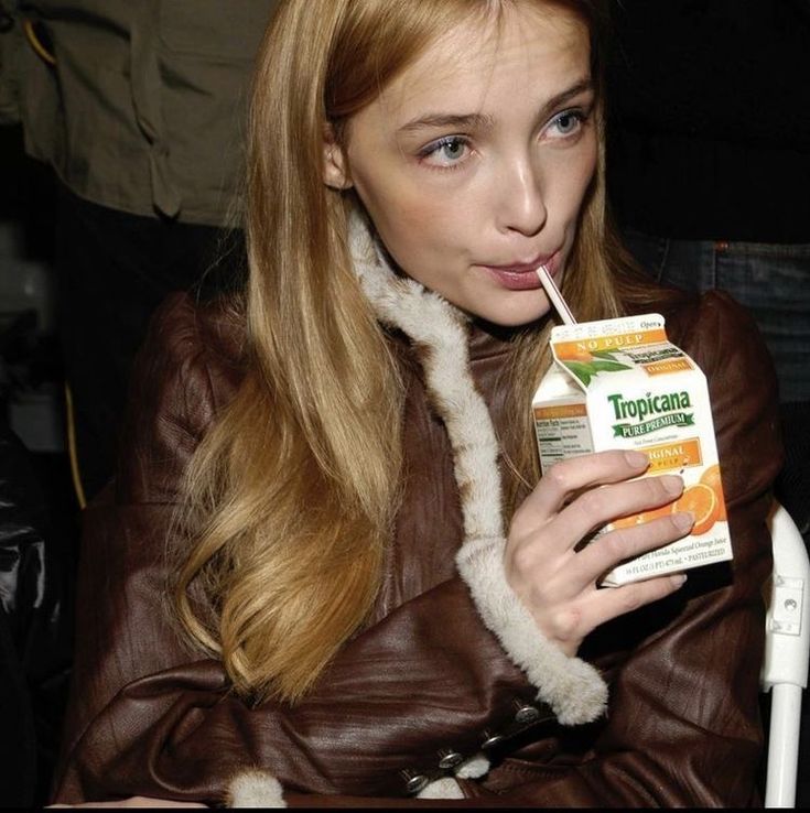 a woman in brown jacket drinking from a carton