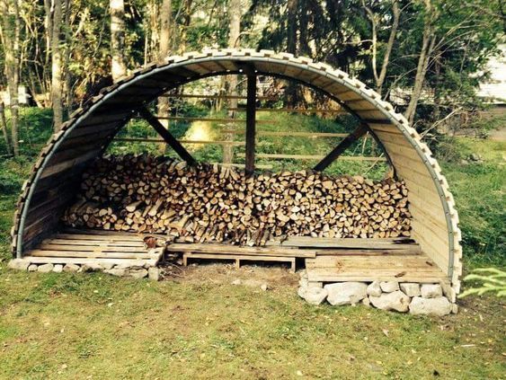 a large pile of firewood sitting inside of a wooden shelter on top of a lush green field