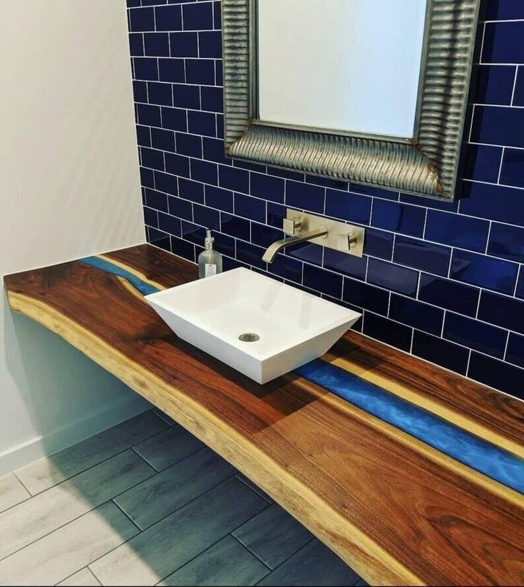 a bathroom with blue tile and wooden counter top, square white bowl sink on wood planks