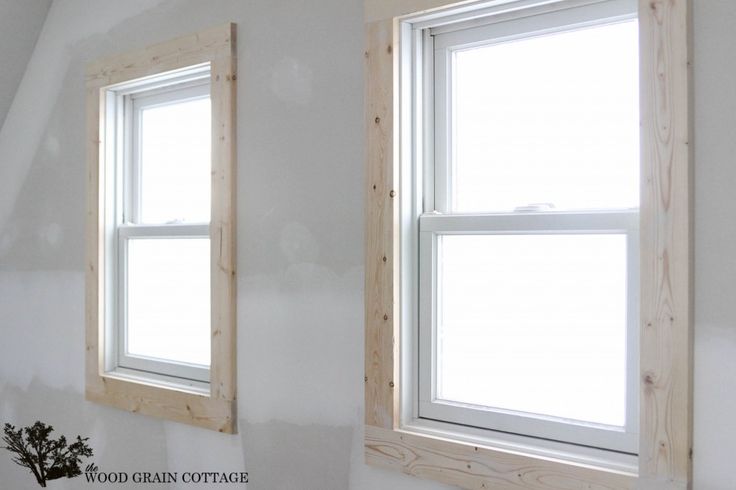 two windows are shown in the corner of a room with white walls and wood trim