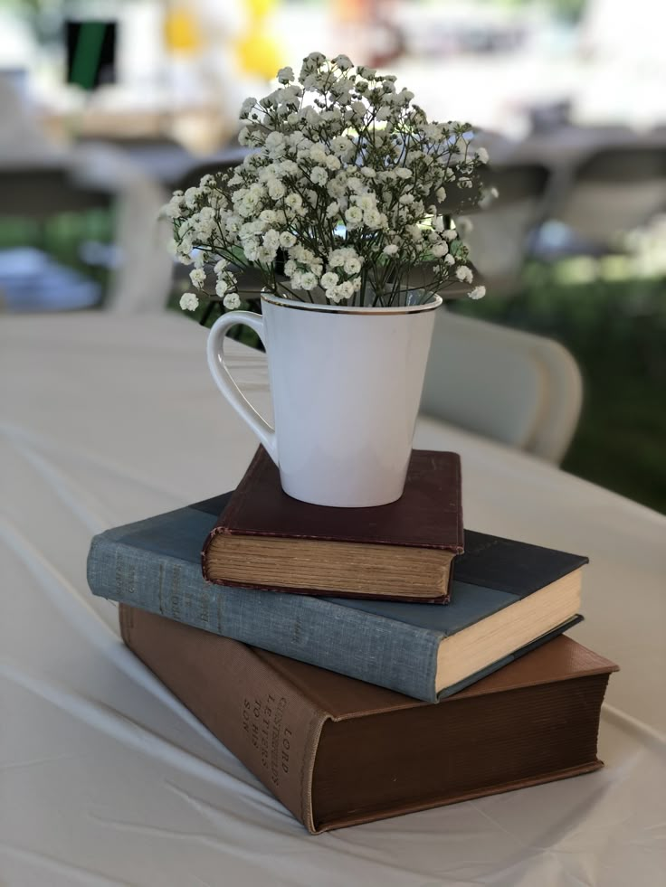 three books stacked on top of each other with a white cup filled with baby's breath