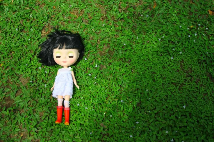 a doll is laying in the grass with red boots on it's feet and black hair