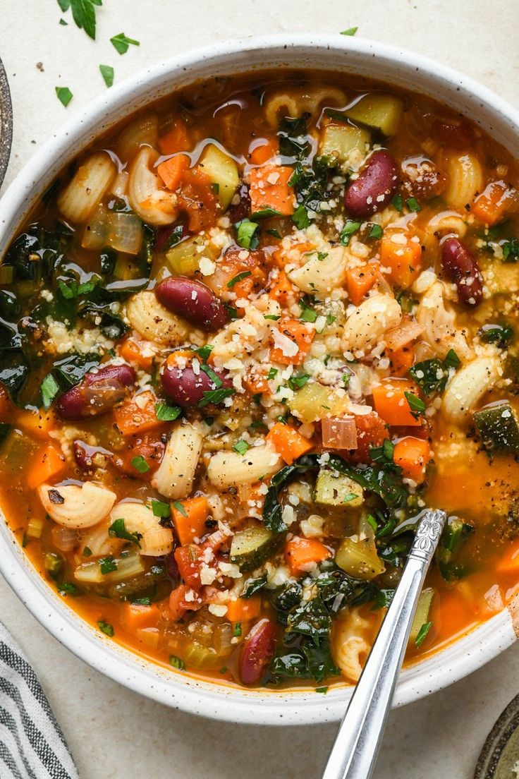 a white bowl filled with vegetable soup and some silver spoons on top of it