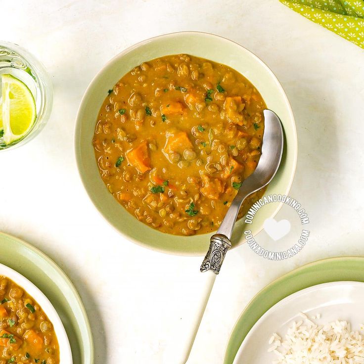 there is a bowl of soup on the table next to two plates with rice and limes