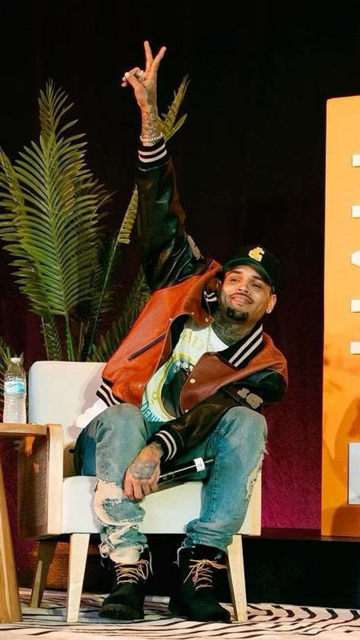 a man sitting on top of a white chair in front of a table with a plant