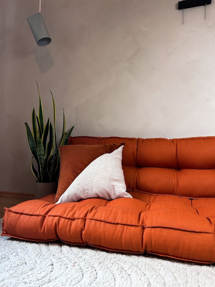 an orange couch with a white pillow on top of it next to a potted plant