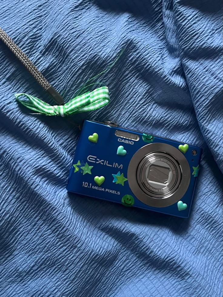 a blue camera sitting on top of a bed next to a green and white scarf