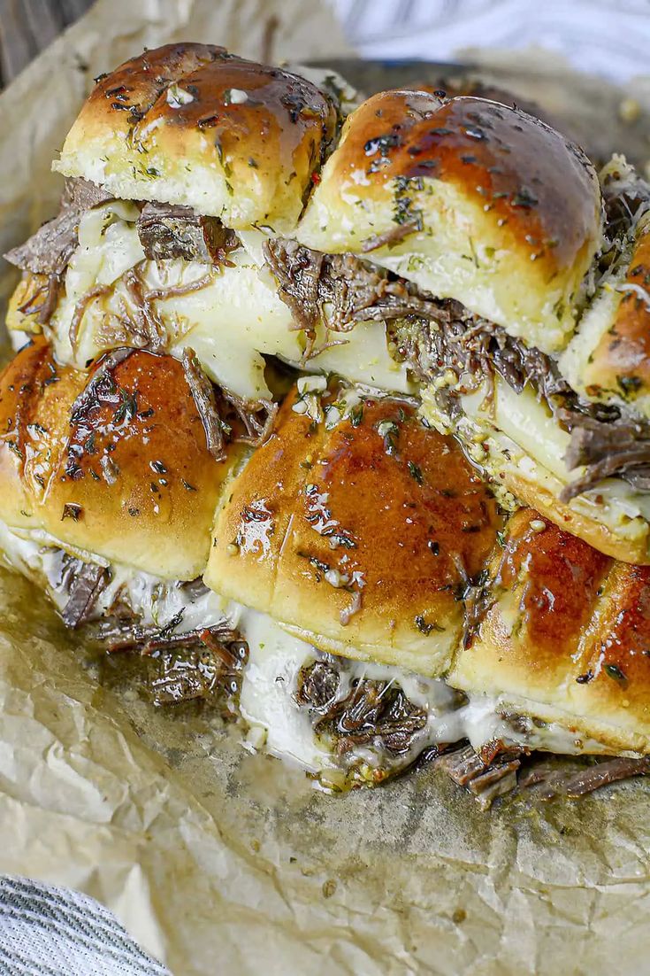 a pile of sliders covered in cheese and meat sitting on top of wax paper