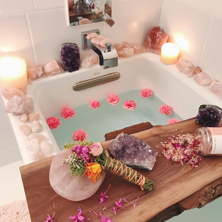 a bathtub filled with flowers and candles next to a wooden table topped with rocks