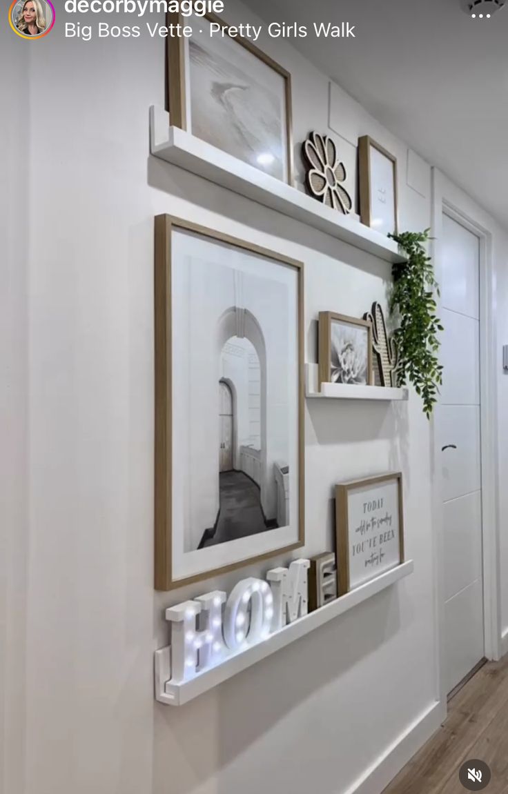 a white wall with some pictures and frames on the wall next to it is a plant