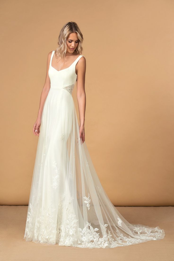 a woman in a white wedding dress standing on a beige background with her back to the camera