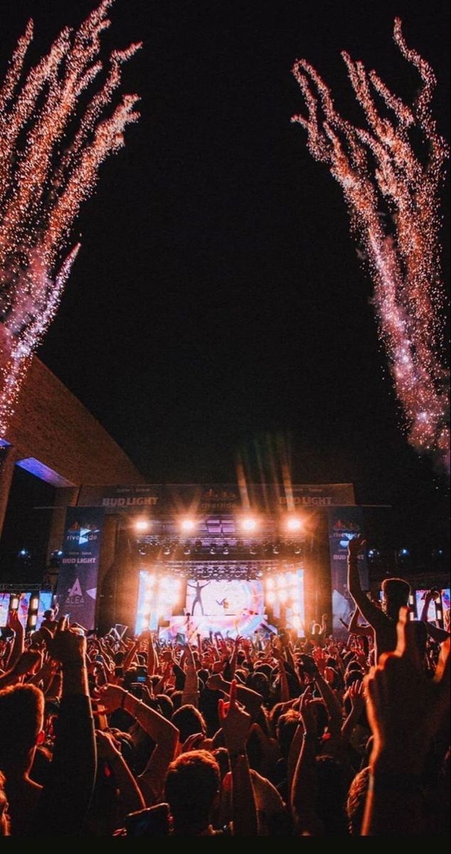 fireworks are lit up in the night sky as people watch from their seats at an outdoor concert