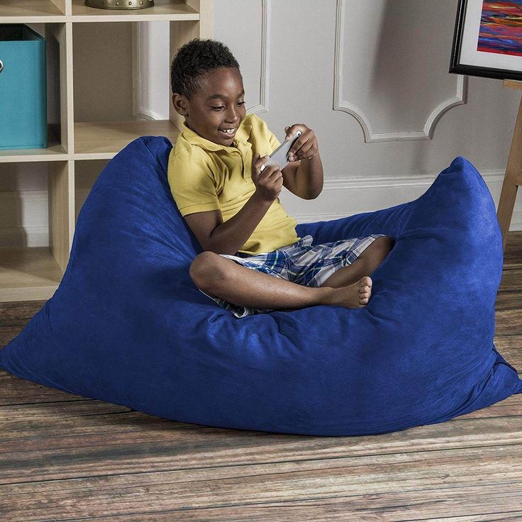 a young boy sitting on a blue bean bag chair in front of a bookcase