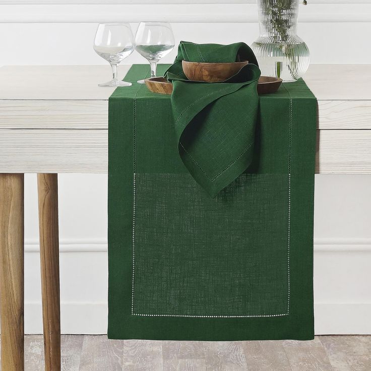 a green table cloth with white stitching on it and two wine glasses in the background