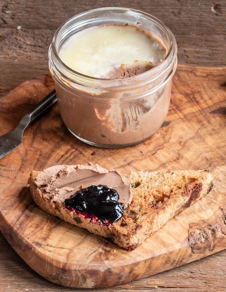 a wooden cutting board topped with a sandwich next to a jar of pudding